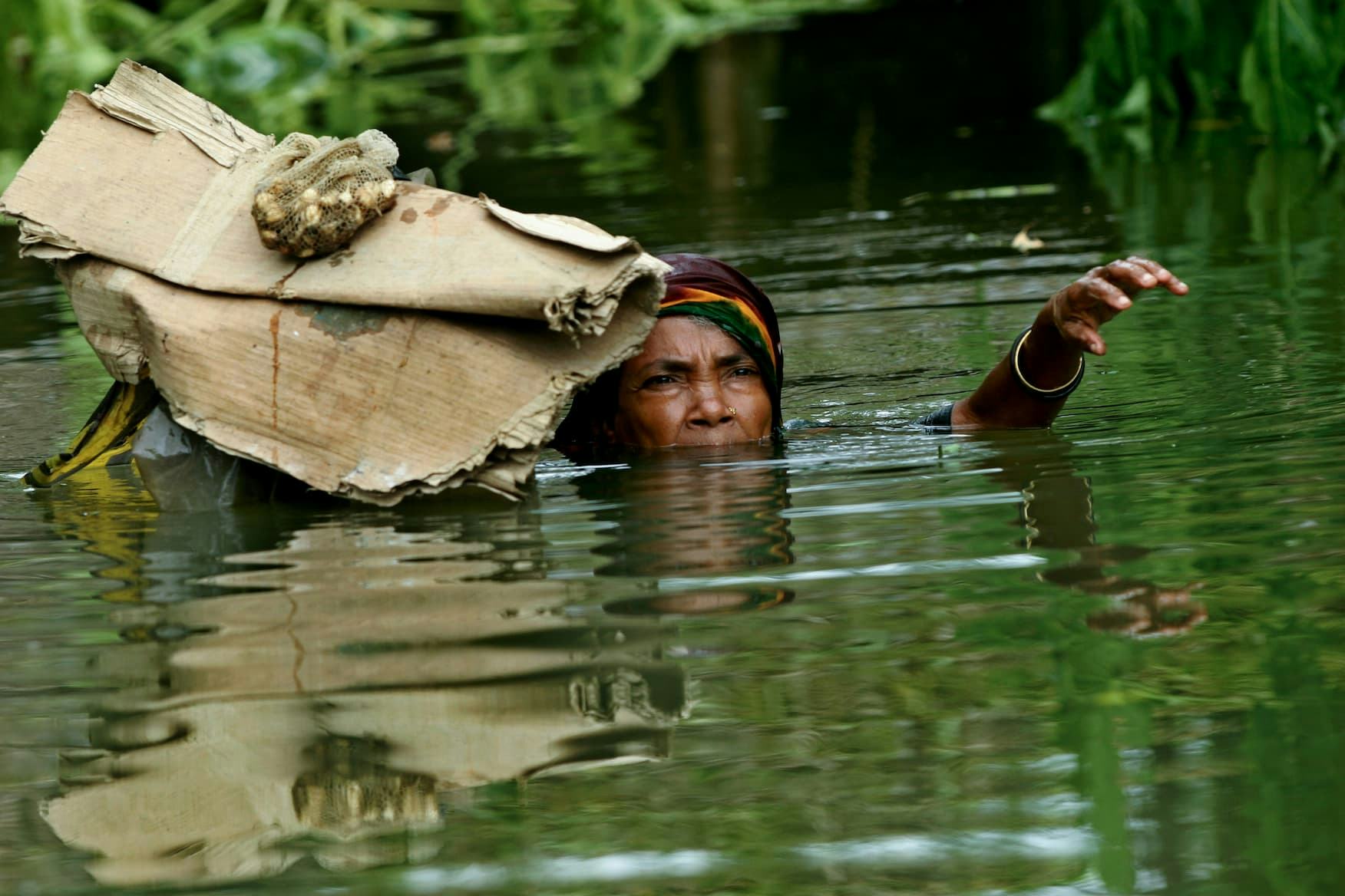 A flood victim wades through deep water as she has managed to salvage the daily cooking essentials from her home which has already gone under water. Sariakandi, Bogra, Bangladesh