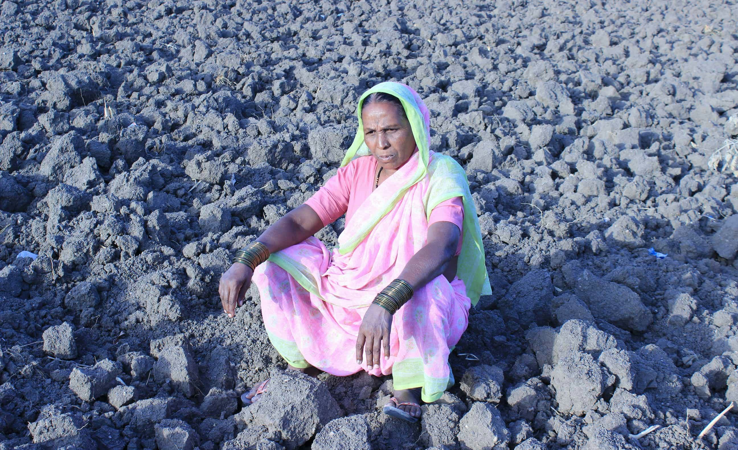 An elderly lady sitting in her arid farm fields brought about by drought, India